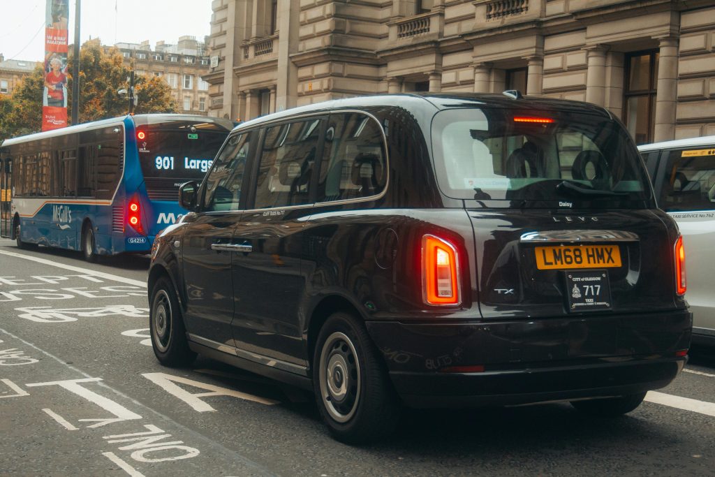 A picture of a taxi being driven in a busy town centre